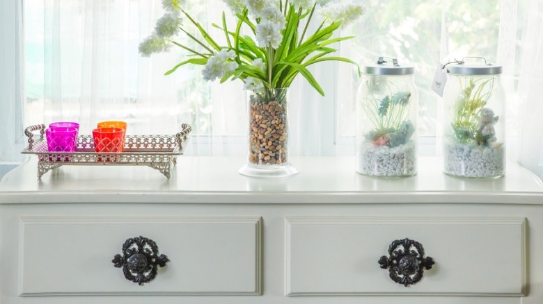 Üstünde bitki ve dekor bulunan beyaz bir şifonyer