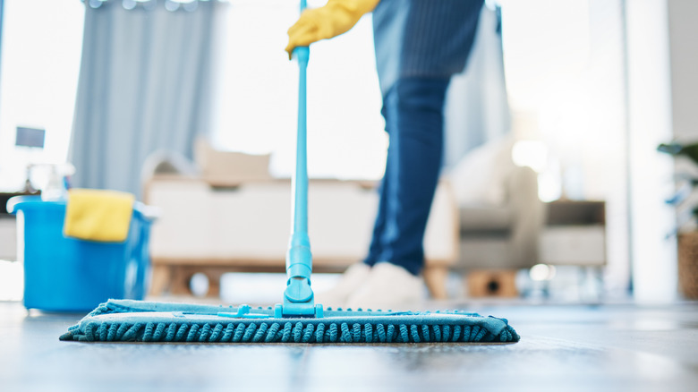 Evdeki boyalı ahşap zeminde mikrofiber paspas kullanan kişi