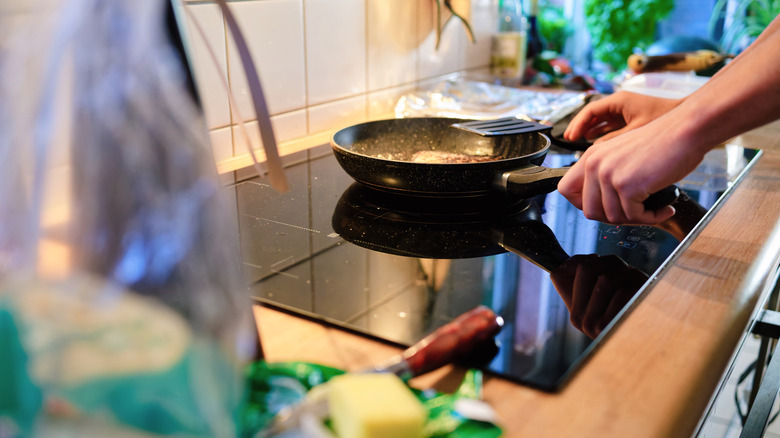 İndüksiyonlu ocakta kızartma tavasında yemek pişiren kişi