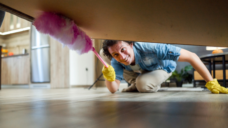 Bir kişi pembe toz beziyle yatağın altını temizliyor