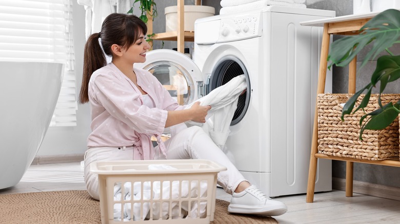 Çamaşır makinesinin yanındaki kıyafetleri inceleyen kadın