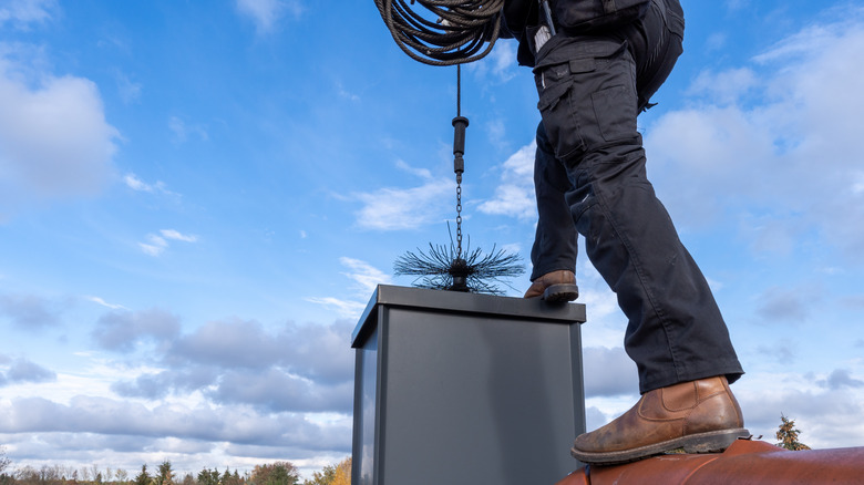 Baca temizleyicisi çatıda duruyor, açık bir günde ekipmanlarını bacadan aşağı indiriyor
