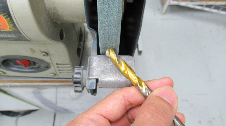 Tezgah öğütücüde matkap ucunu keskinleştiren bir el.