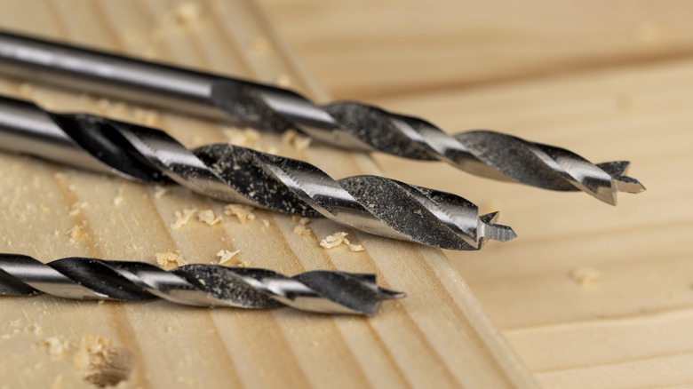 Çam tahtasına delik açtıktan sonra testere tozuyla metal matkap uçları.