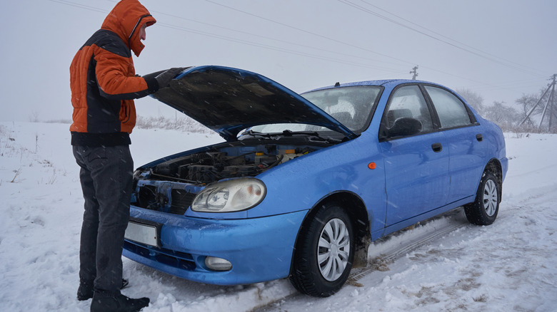 karda bozulan arabanın kaputunun altına bakan kişi