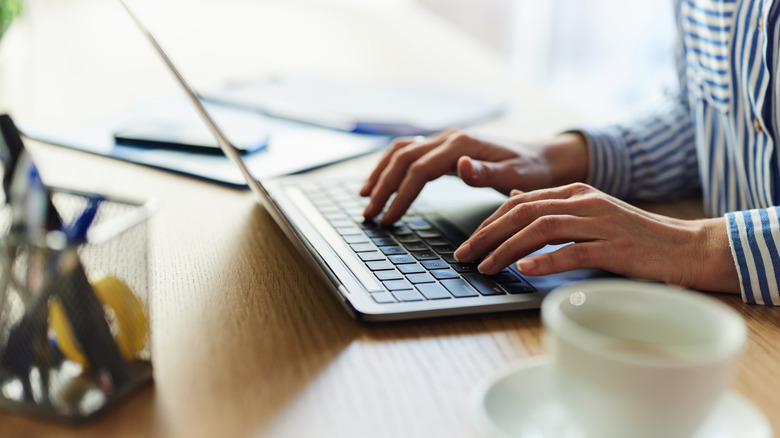 Mavi beyaz çizgili gömlek giyen bir kişi dizüstü bilgisayar kullanıyor