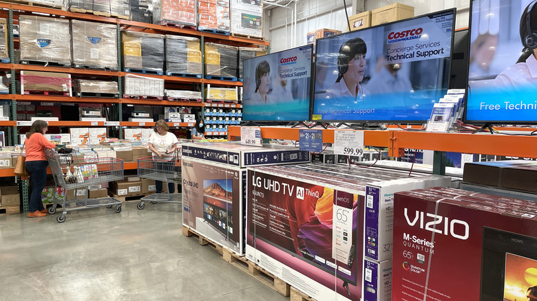 Costco'da televizyon koridorunun yakınında alışveriş yapan insanlar