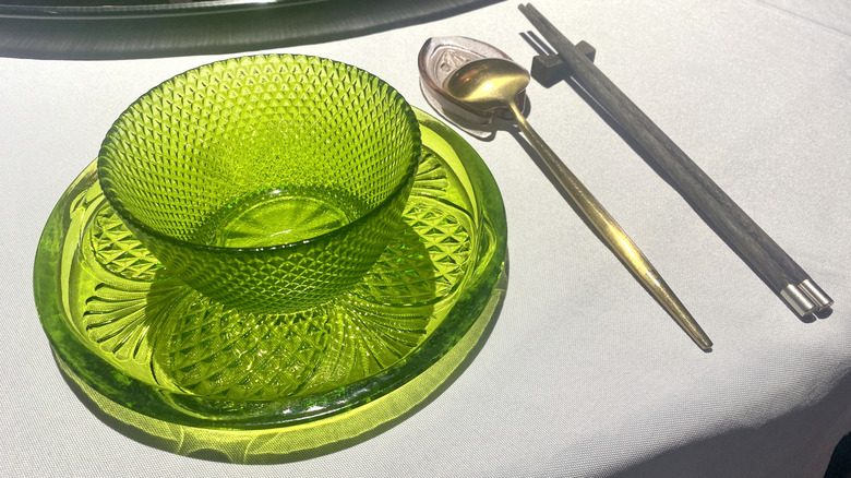 Kaşık ve yemek çubuklarının yanındaki tabakta yeşil cam kase