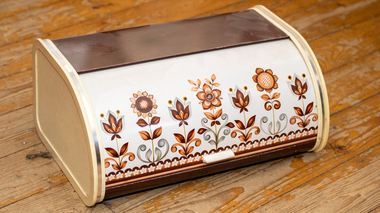 Ahşap bir masanın üzerinde eski bir metal ekmek kutusu.