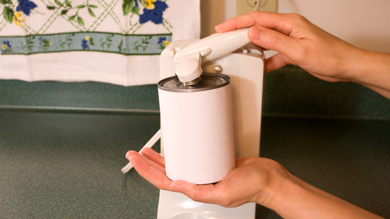 Bir kişi eski bir elektrikli konserve açacağı kullanarak konserveyi açıyor.