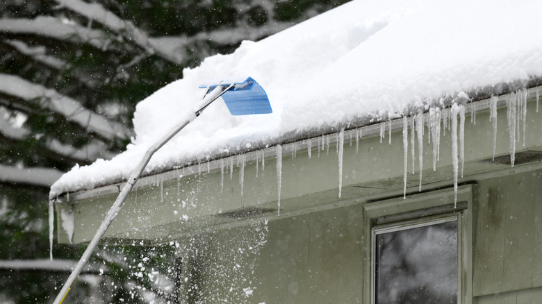Kar kaldırmak için kar çatı tırmığı kullanan kişi