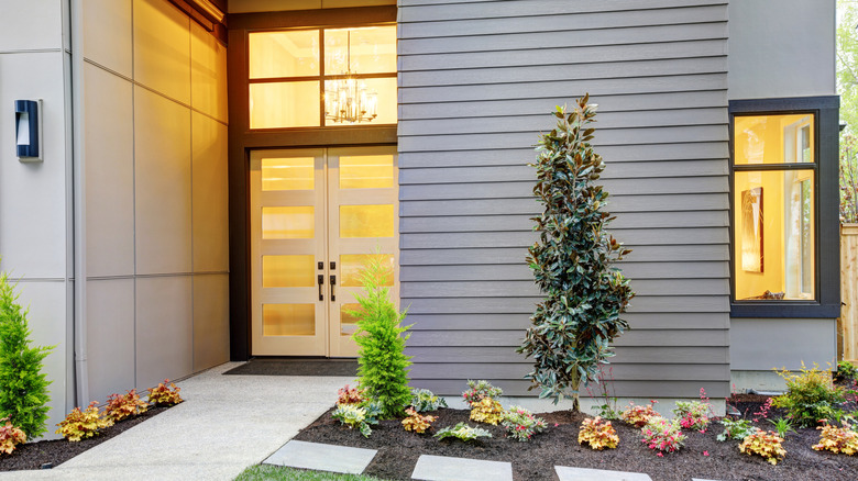 Modern çift ön kapısı, pencereleri ve bahçesi olan bir evin önü.