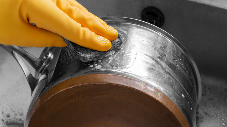 Lastik eldiven giyen, paslanmaz çelik ve bakır tencereyi tel pedle temizleyen kişi.