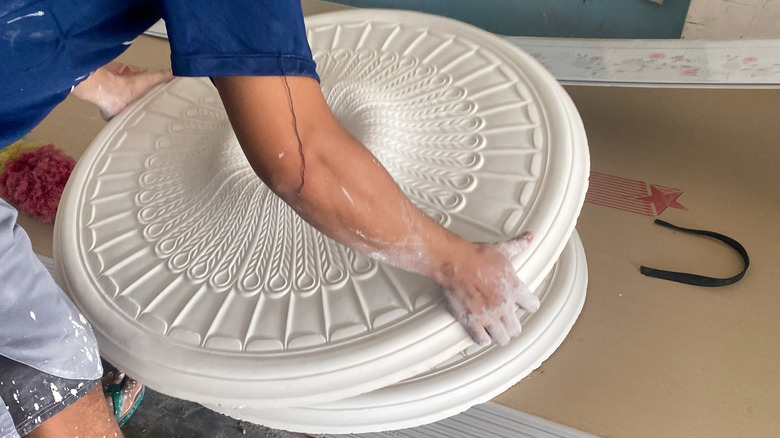 Bir kişi büyük beyaz bir tavan madalyonunu tutuyor