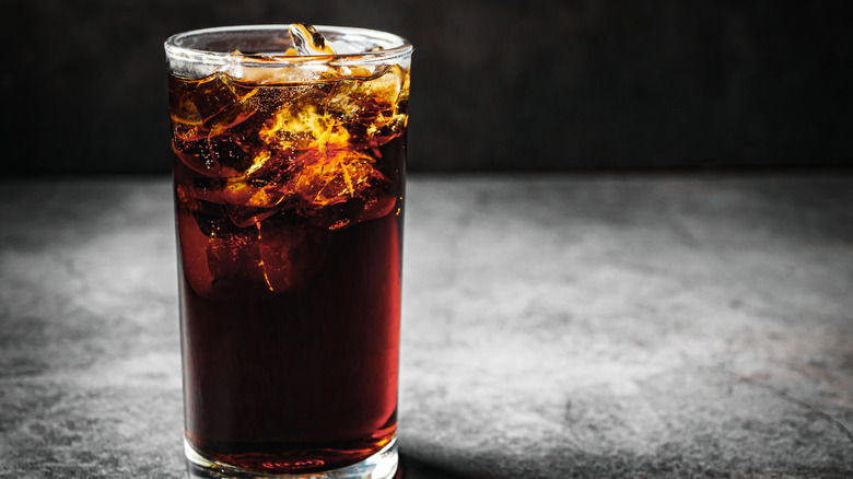 Karanlık arka planı olan bir masada buzlu bir bardak koyu soda