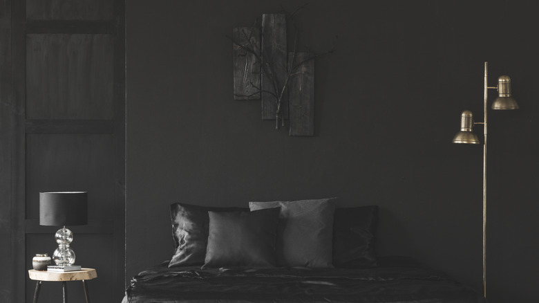 Yan tarafında altın rengi bir lamba bulunan tamamen siyah bir yatak odası.