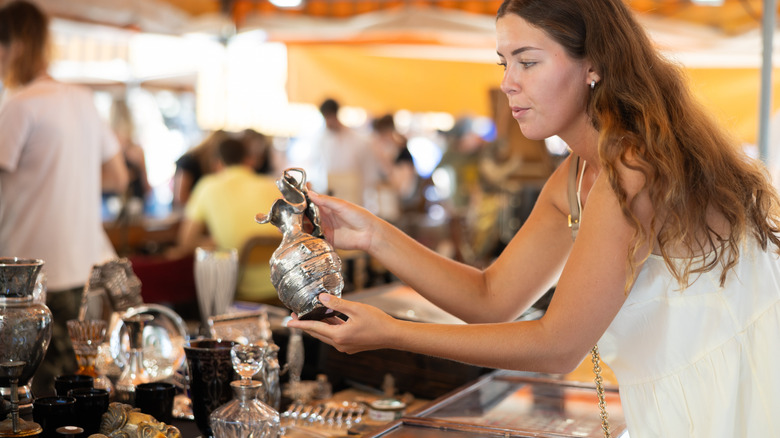 Bir kadın ikinci el pazarında antika bir eşya tutuyor