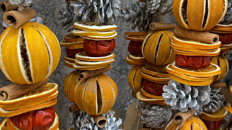 Kurutulmuş meyve ve çam kozalaklarından oluşan çelenkler kağıtla kaplı bir duvara asılıyor.