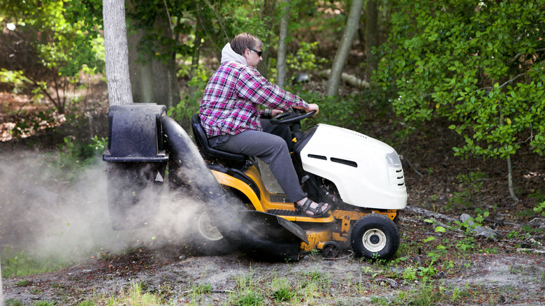 Sigara içen çim biçme makinesi kullanan kişi
