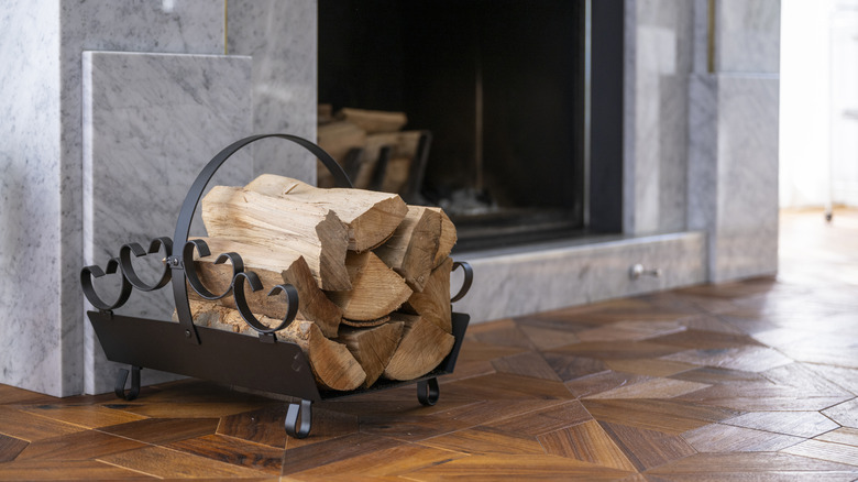 Mermer şöminenin yanında oturan siyah metal yakacak odun tutucusu