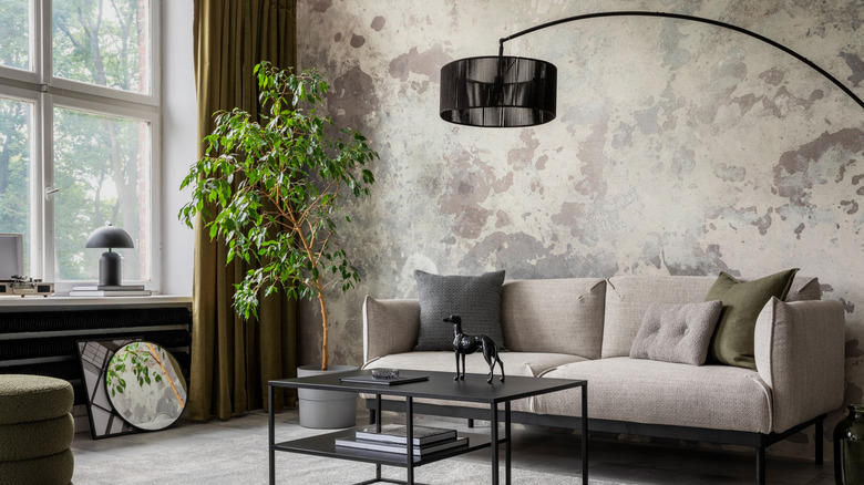 Gri bir kanepe, siyah sehpa ve nötr desenli duvar kağıdı içeren bir oturma odası