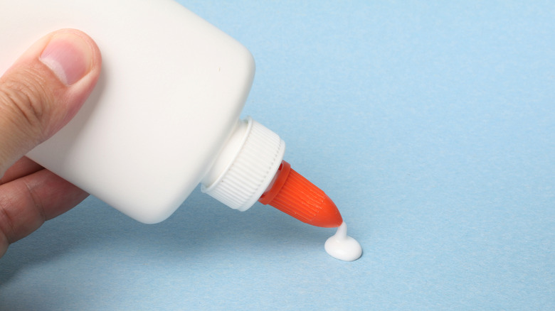 Bir el, açık mavi bir kağıt parçasının üzerine zanaat yapıştırıcısını sıkıyor.