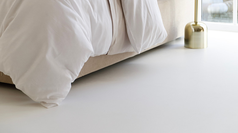 Kalın yorganlı, çok sayıda yastık ve yan sehpadaki vazoda çiçeklerle donatılmış rahat, konforlu yatak