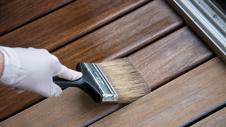 Eldivenli el boya fırçasıyla ahşabı boyuyor