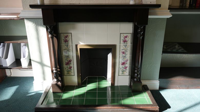 Koyu renkli ahşap, beyaz ve çiçek desenli fayanslar ve yeşil fayanslı şöminenin güçlü olduğunu gösteren güneşli bir iç mekan görüntüsü.