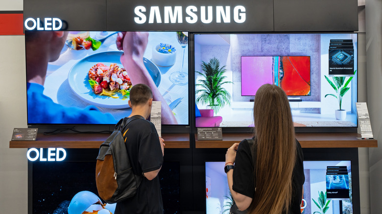 Bir mağazadaki Samsung TV ekranına bakan iki kişi