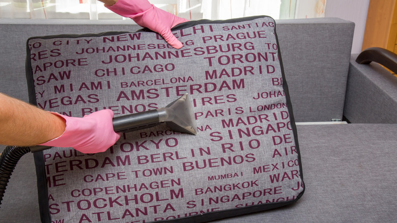 Pembe eldivenli eller kanepedeki dekoratif yastığı süpürüyor.