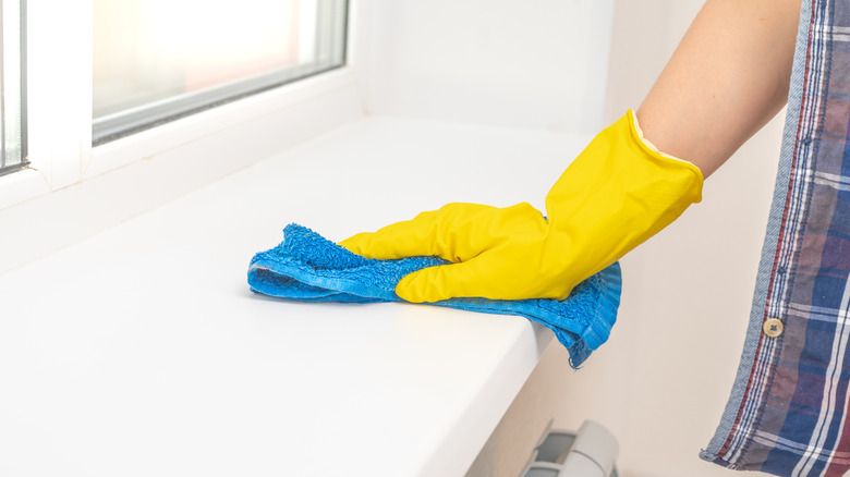 Eldivenli bir el, yan masayı mikrofiber bir bezle siliyor.