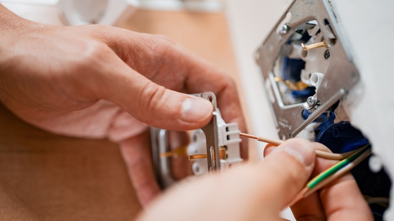 Kabloları yeni bir elektrik prizine dikkatlice bağlayan bir elektrikçinin ellerinin yakından görünümü
