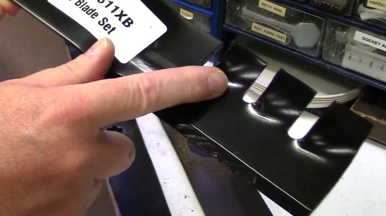 Biçme makinesi bıçağındaki kesici dişleri işaret eden kişi