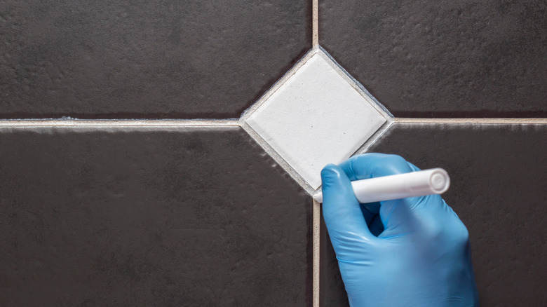 Fayans üzerinde harç kalemi kullanan eldivenli el