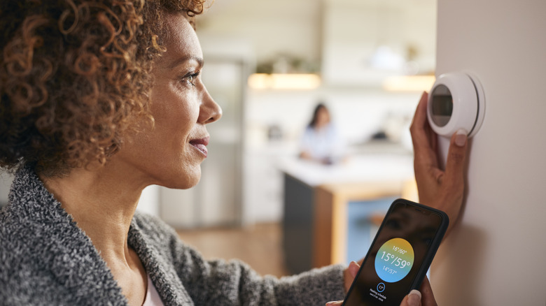 Evde Dijital Merkezi Isıtma Termostatını Kontrol Etmek İçin Telefondaki Uygulamayı Kullanan Kadın