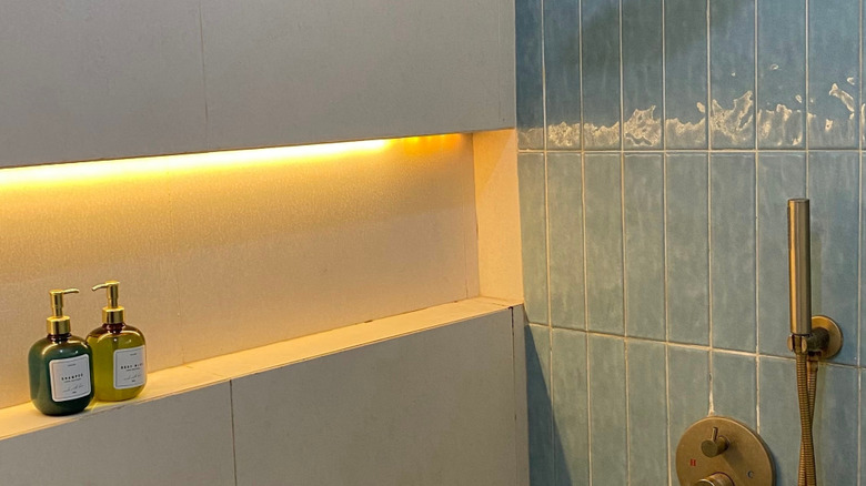Rahat Banyo Ortamında Pirinç Armatürler, Mavi Duvar Fayansları ve LED Raf Aydınlatması ile Modern Minimalist Duş İçi. Jogja, Endonezya, 25 Mayıs 2025