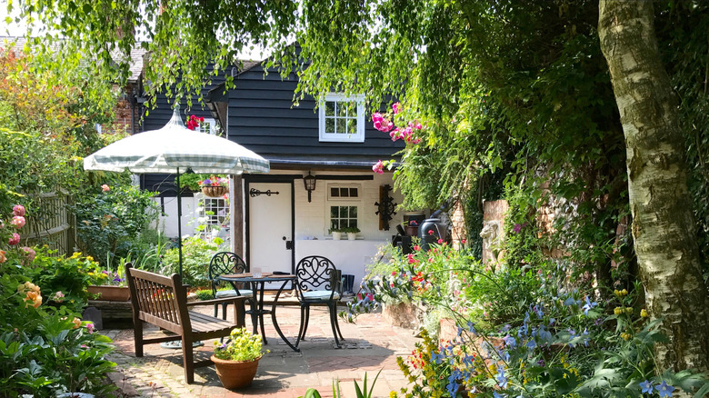 Masa, sandalyeler, şemsiye ve bolca bitki örtüsünün olduğu yemyeşil bir arka bahçe