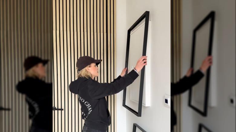 Bir kişi duvardaki bir malzeme kutusunun üzerine IKEA resim çerçevesini asıyor.