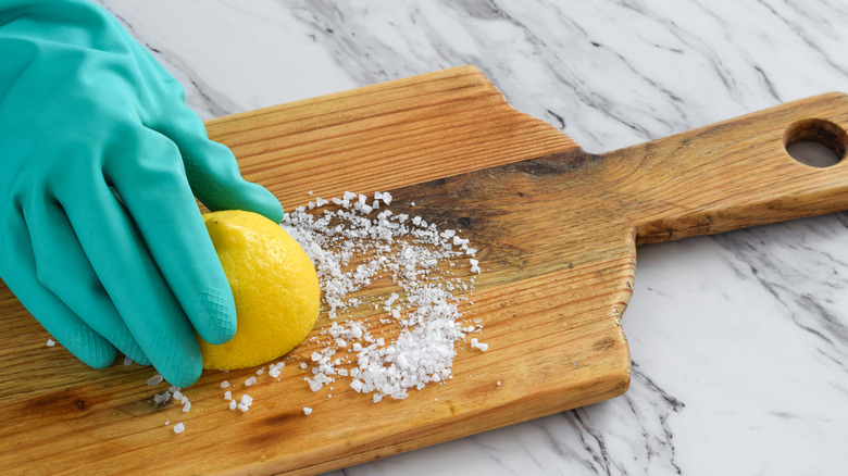 mavi eldivenle yarım limonu tuza basan kişi
