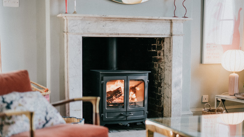 Beyaz şömine, ocakta odun sobası ve mermer şömine rafı.