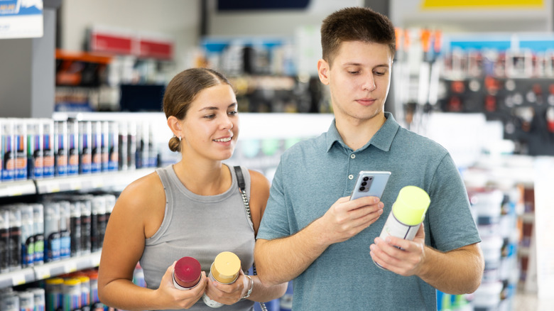 Genç bir çift, bir hırdavatçıdaki sprey boya şişelerini taramak için telefon kullanıyor