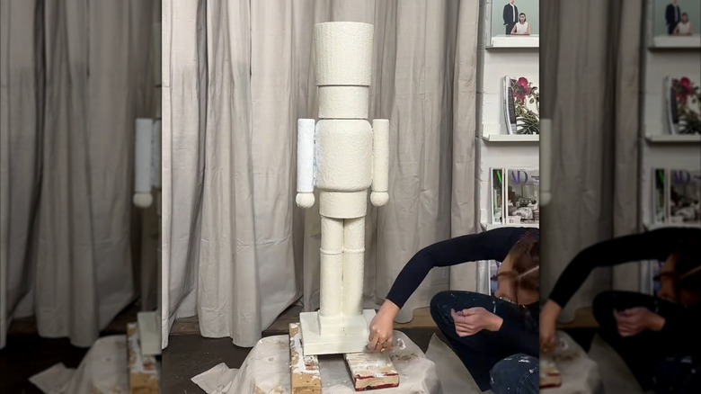 Ahşap bir taban üzerine cips kutuları, teneke kutular ve tenis toplarından yapılmış uzun bir oyuncak askeri boyayan kadın