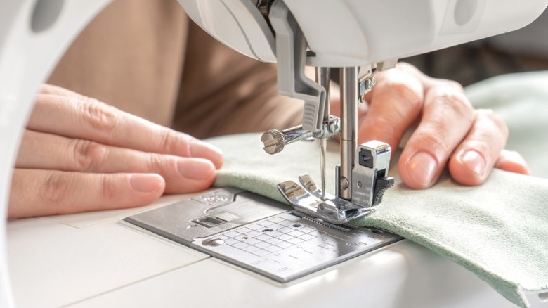 Kumaş kapak tutucusu yapmak için kumaşın kenarını dikiş makinesiyle kıvıran kişi