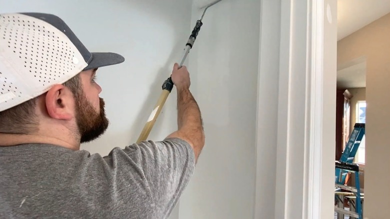 Adam vestiyer duvarına beyaz boya sürüyor