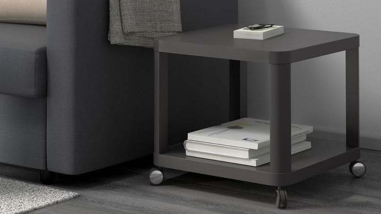 Gözlüklü koyu gri bir kanepenin yanında koyu gri bir TINGBY ve raflarda birkaç kitap var