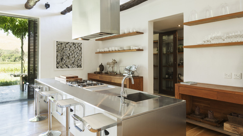 Beyaz duvarlı, ahşap raflı ve paslanmaz çelik mutfak adasına sahip modern mutfak.