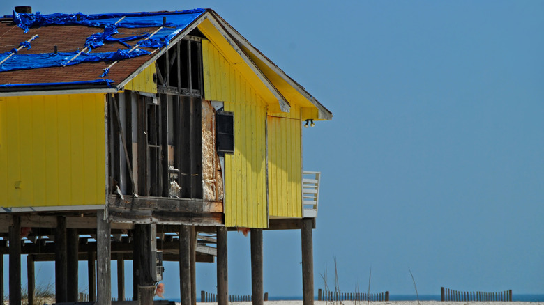 Okyanusun yakınında kazıklar üzerinde rüzgardan zarar görmüş bir ev