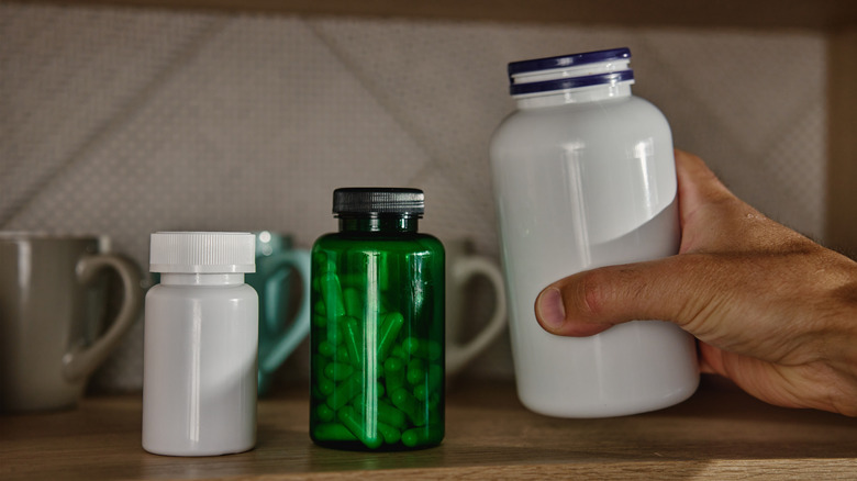 İlaç şişesini kahve kupalarının yanındaki rafa yerleştiren el