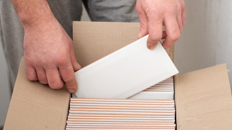 Bir kutu fayanstan açık renkli bir fayans alan kişi.